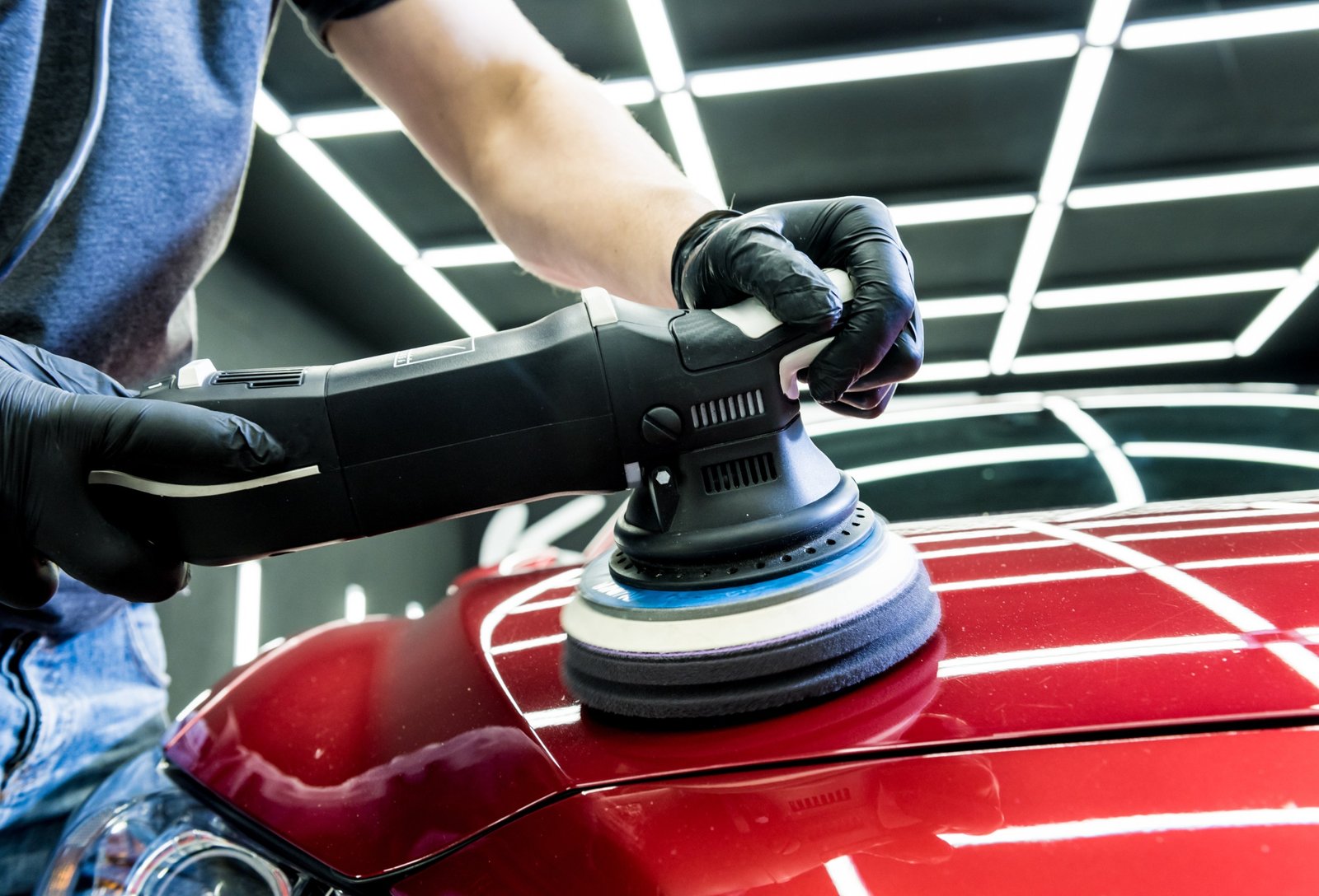 car service worker polishes a car details with orbital polisher.